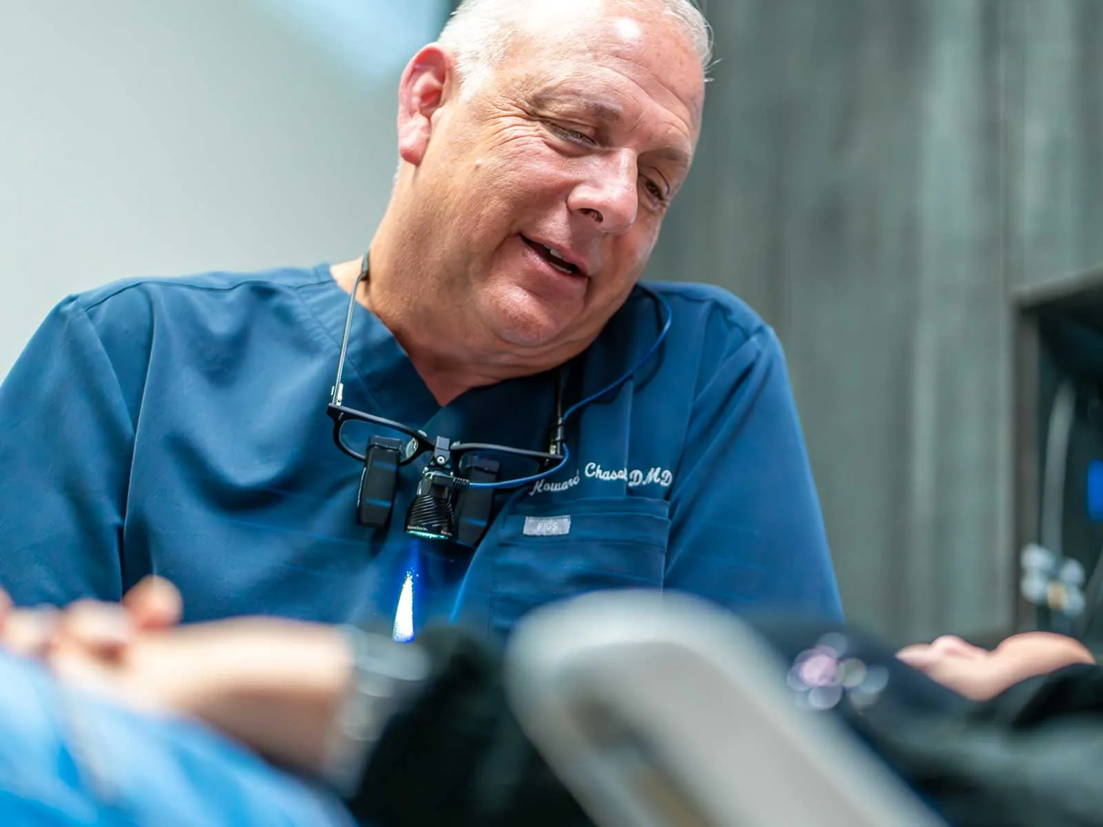 Dentist wearing blue scrubs consulting with a patient in a dental clinic setting.