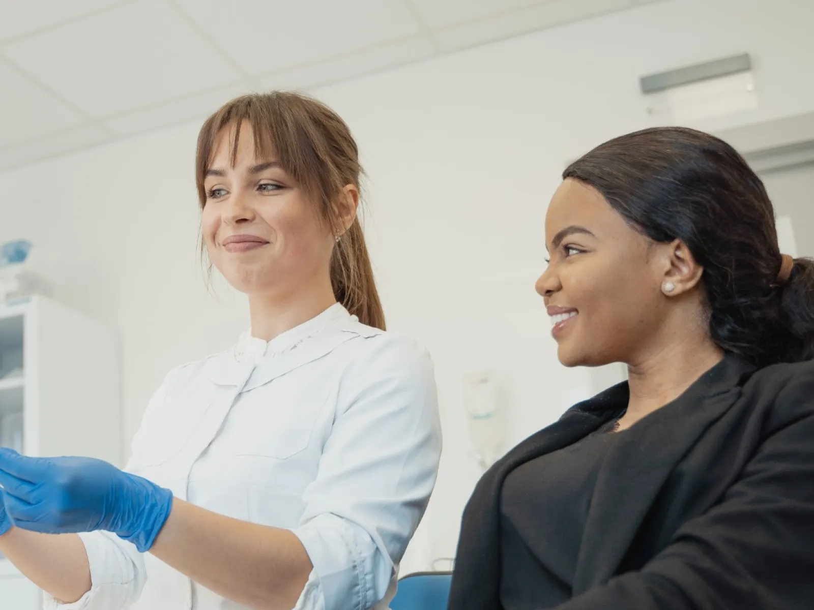Dentist in blue gloves showing dental X-ray on tablet to a seated female patient in clinic