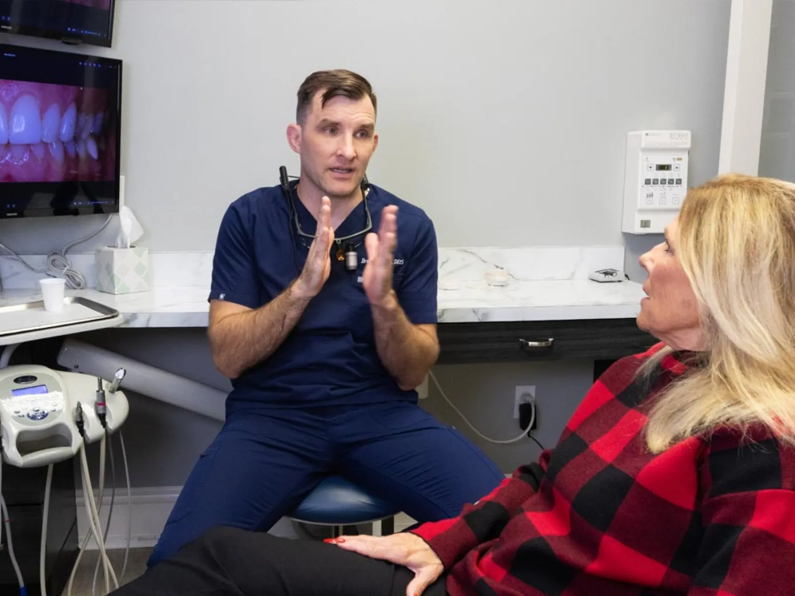 Dentist consulting a female patient in a dental office with oral health images on a screen beside them.