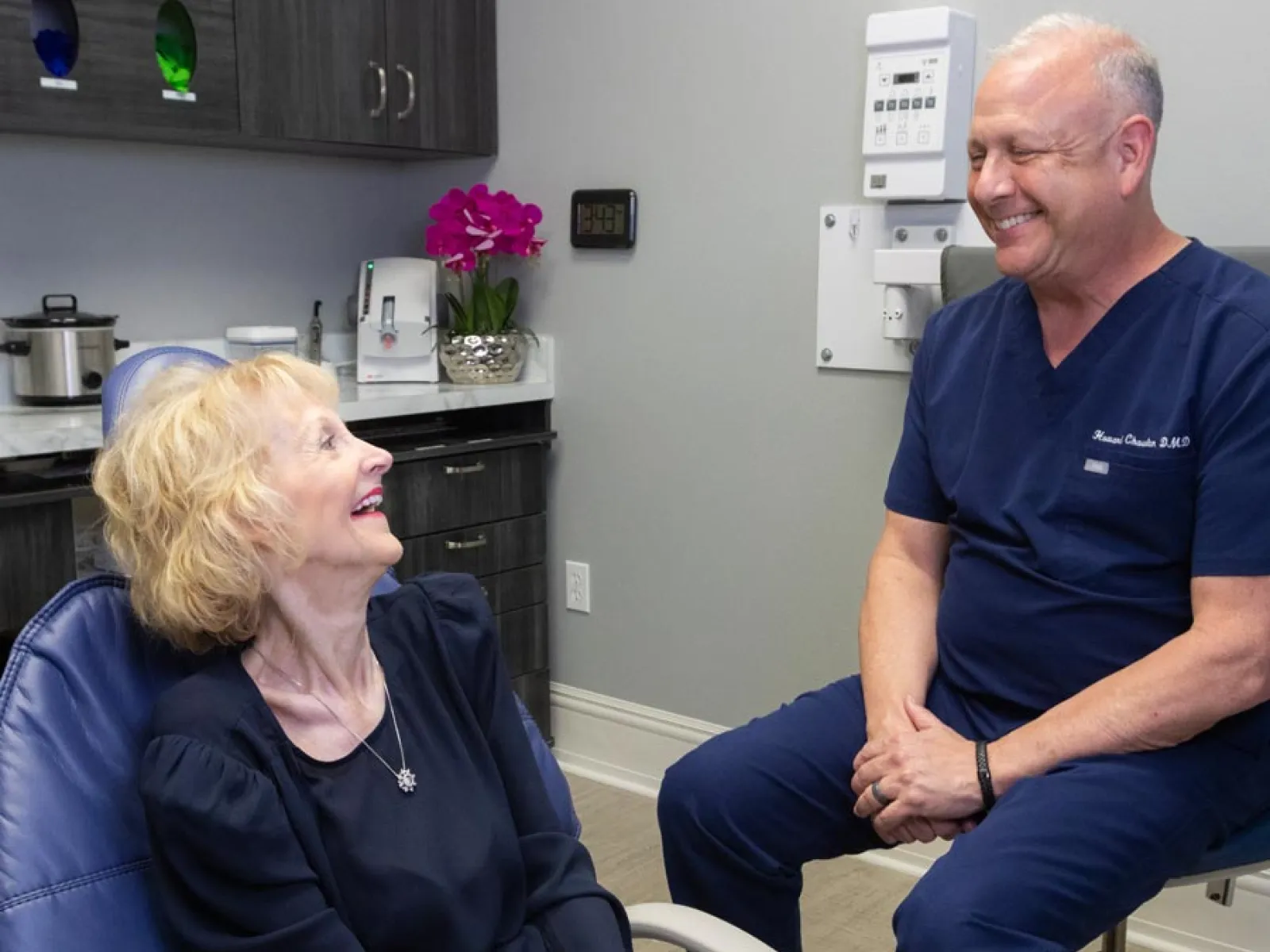 Senior woman smiling and talking with male dentist in a modern dental office setting.
