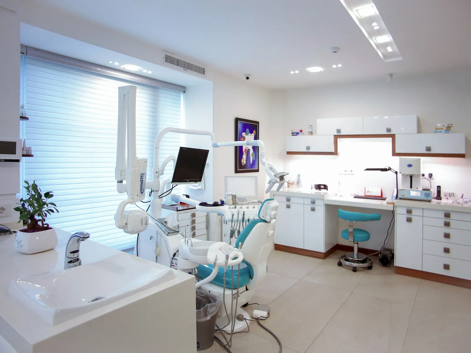 Bright modern dental clinic with dental chair, monitor, sink, and white cabinetry under natural light.