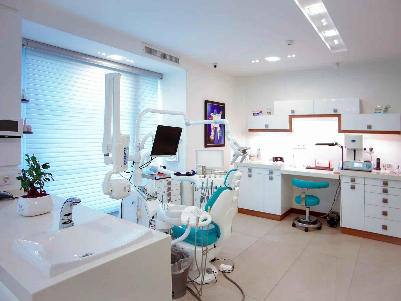 Bright modern dental clinic with dental chair, monitor, sink, and white cabinetry under natural light.