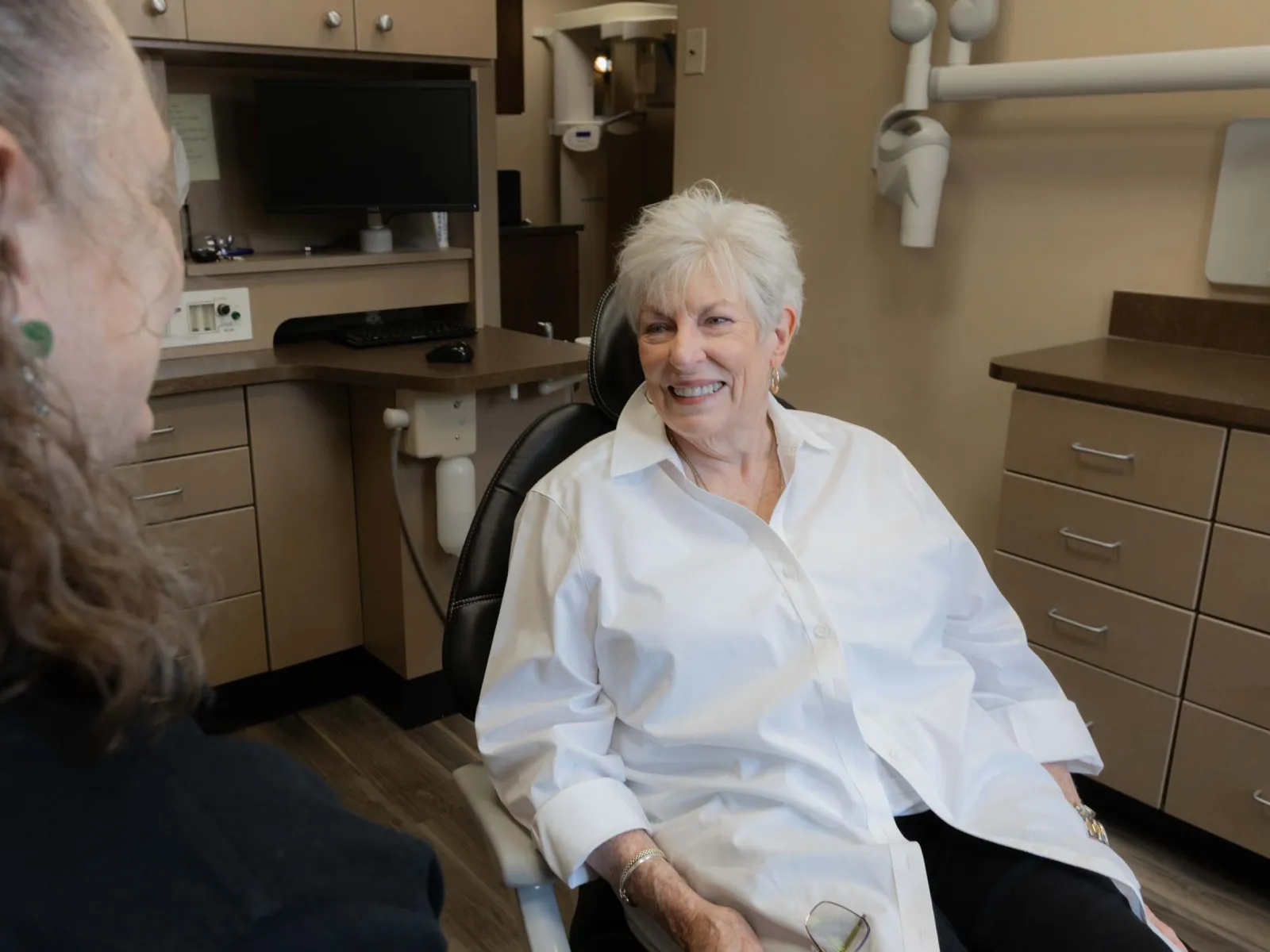 Senior woman smiling in dental chair during consultation with dentist in modern clinic room