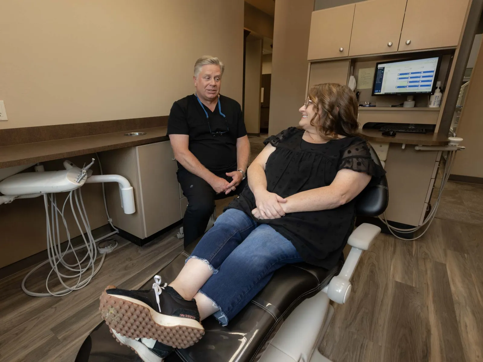 Dentist consulting with female patient seated in dental chair in a modern clinic room.