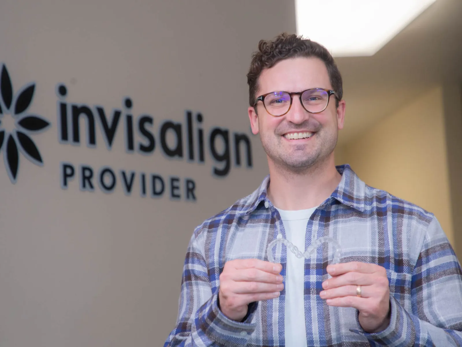 Smiling man holding clear Invisalign aligner in dental office with Invisalign Provider sign in background