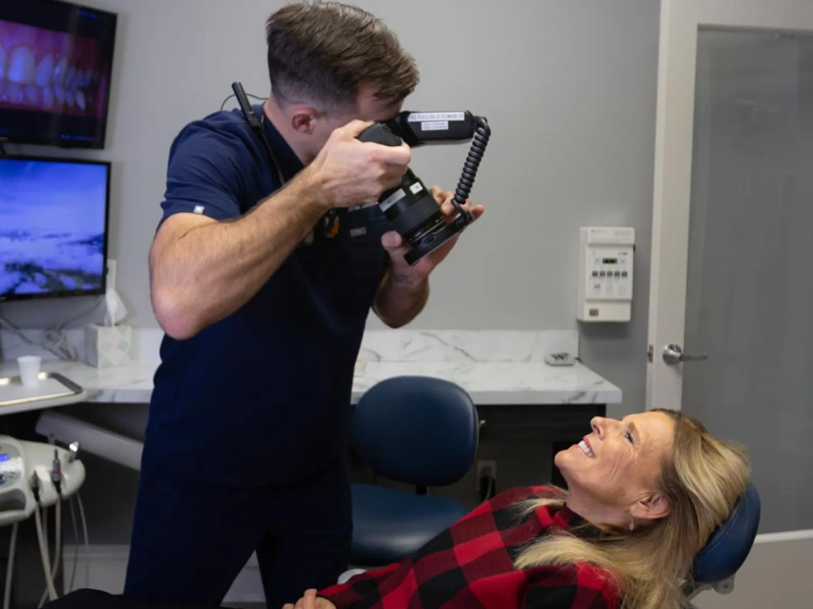 Dentist capturing close-up dental photos of a smiling woman reclined in a dental chair during oral examination.