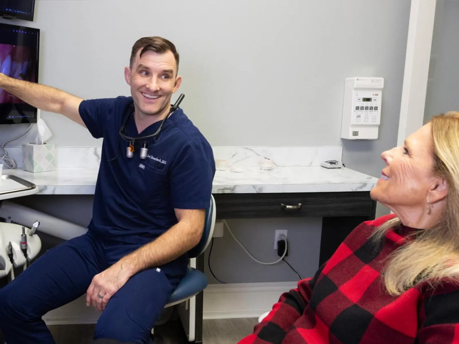 Male dentist explaining dental x-rays on a monitor to relaxed female patient in a modern dental clinic.