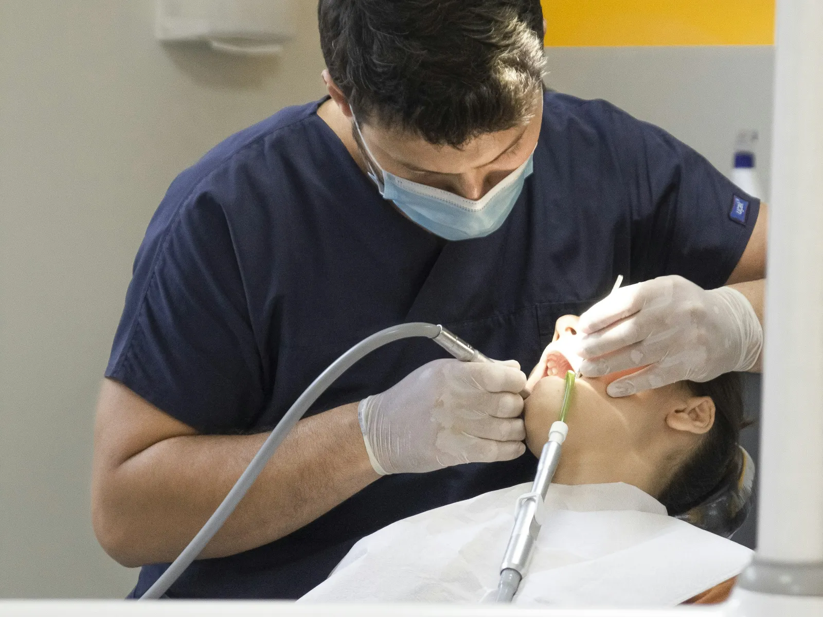 Dentist wearing mask treating patient's teeth using dental tools in a modern clinic.