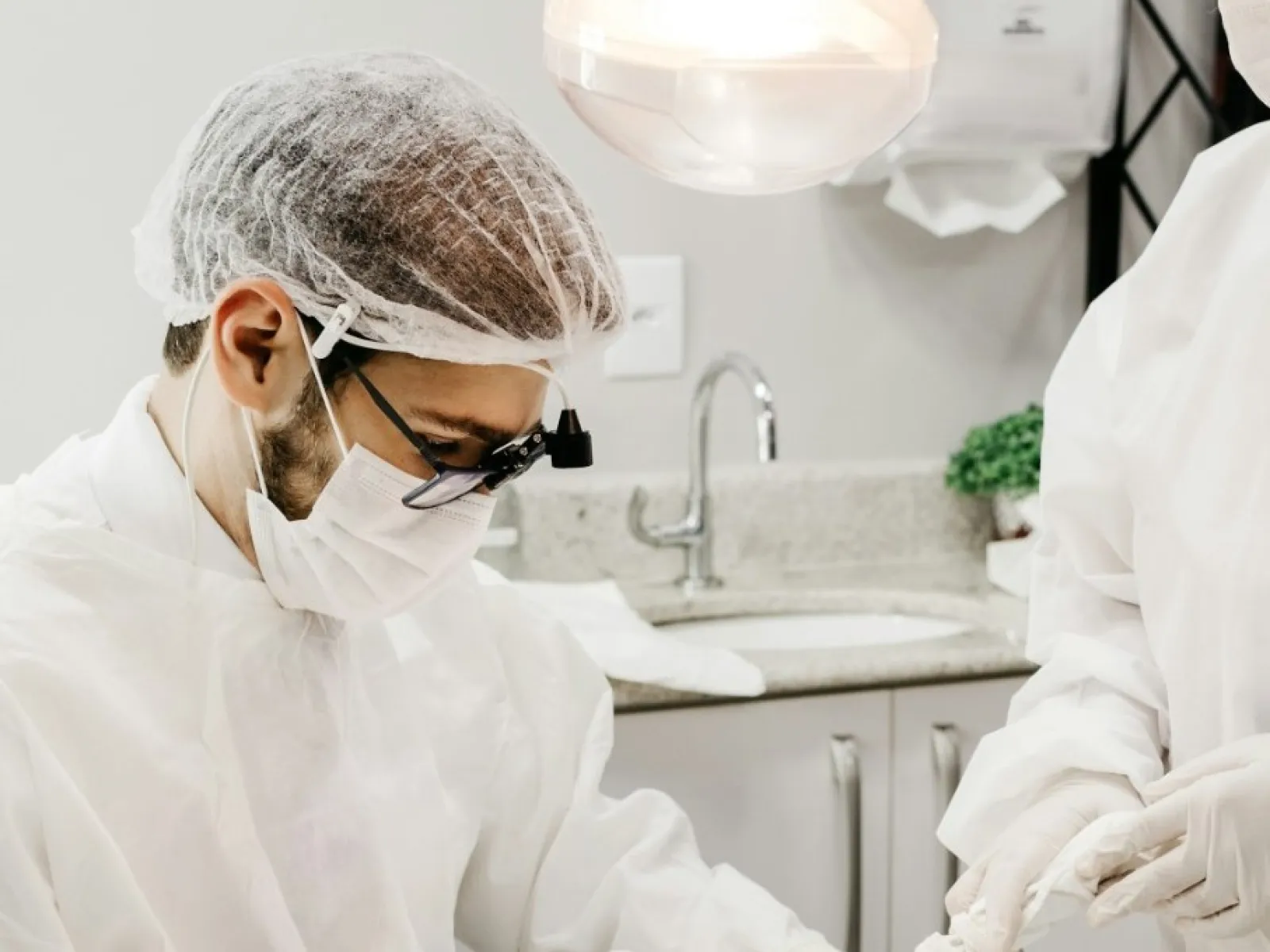 Dentist and assistant wearing protective gear performing dental procedure on patient in clinic.