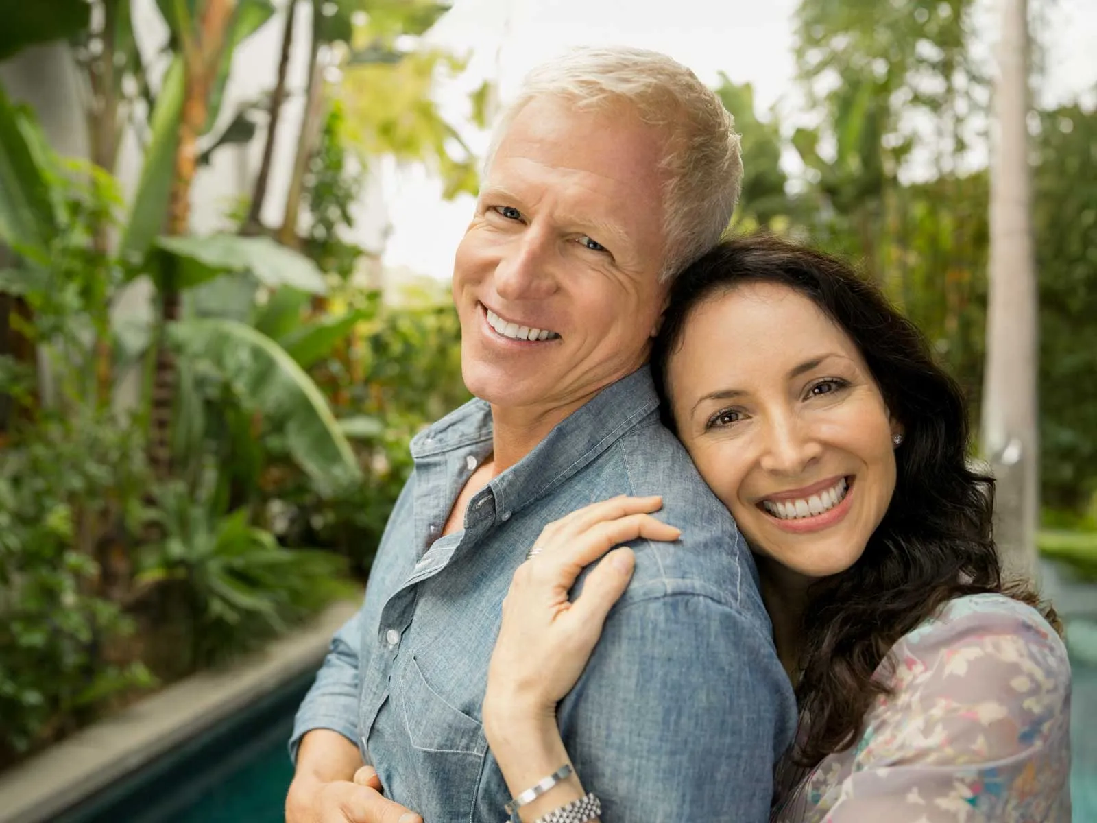 Happy mature couple embracing outdoors in a lush green garden with smiles, showing affection and warmth.