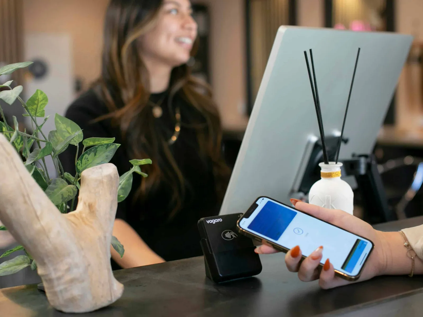 Customer using mobile phone for contactless payment at a salon reception counter with a smiling staff member.