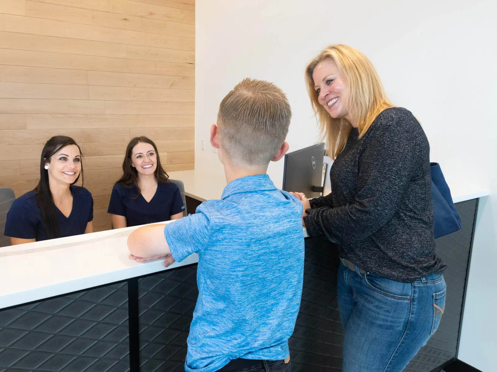 Smiling receptionist staff attending to a woman and her young son at a clean modern front desk.