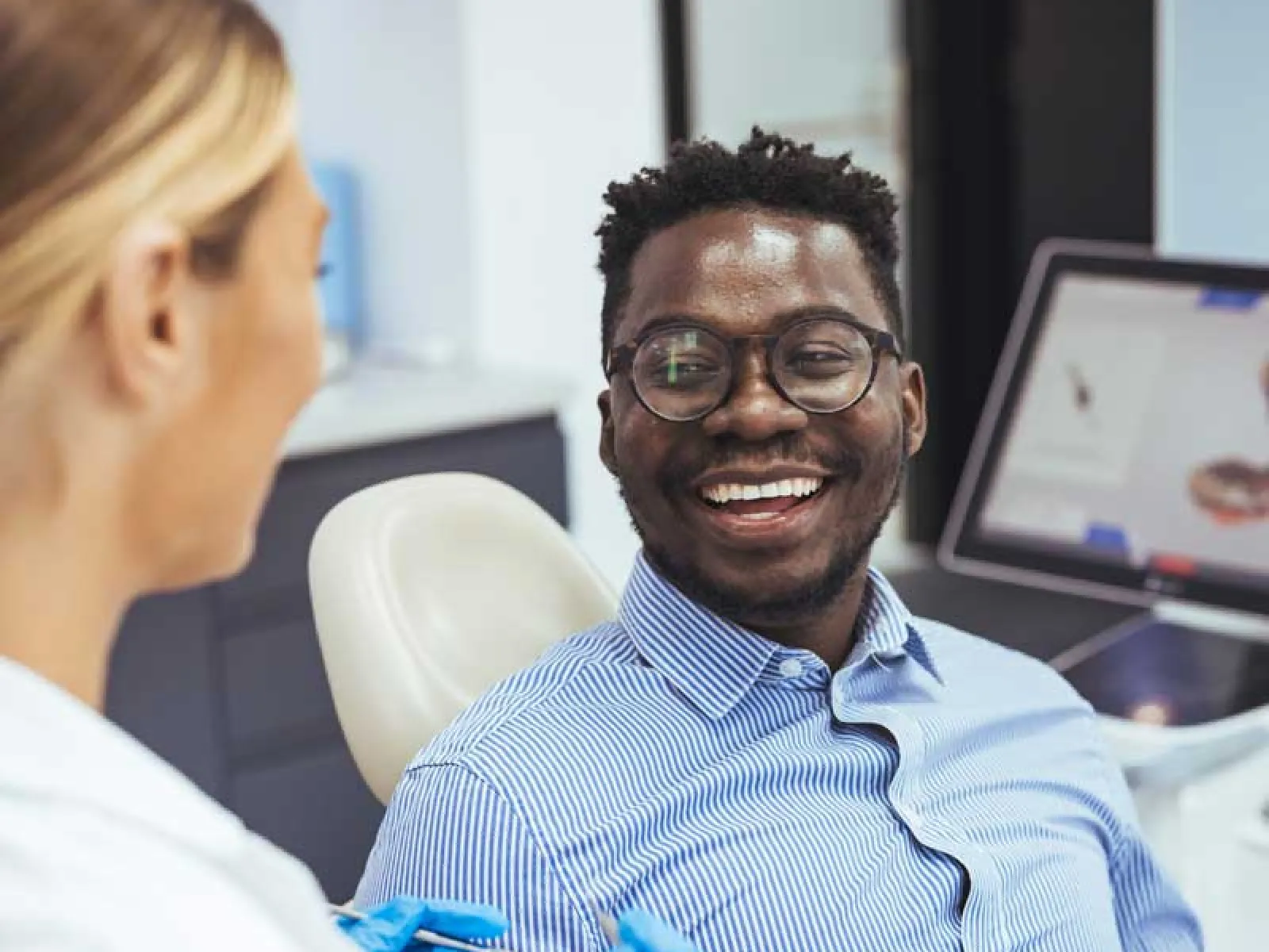 Smiling man wearing glasses in dentist chair engaging with female dental professional in clinic.