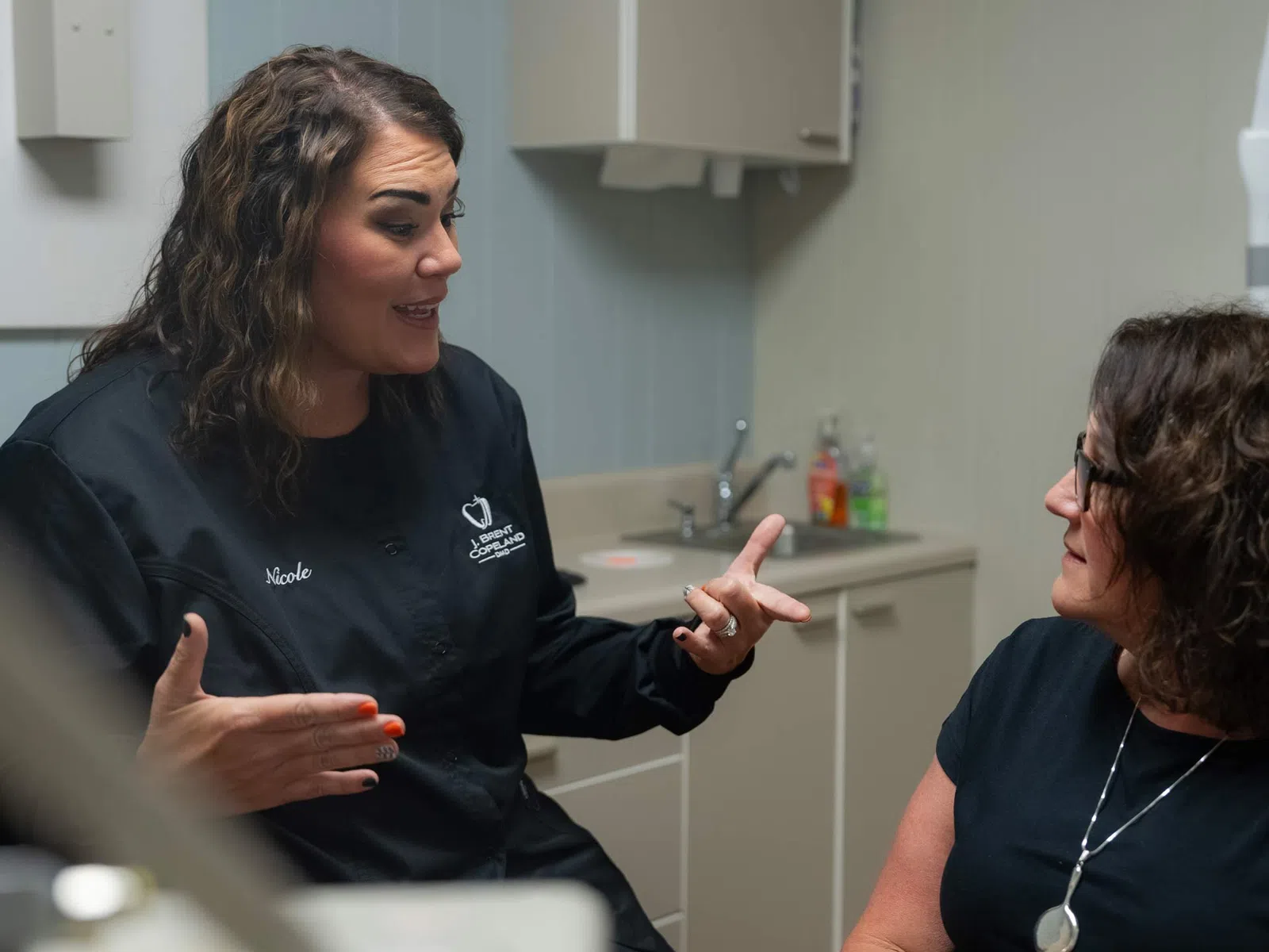 Healthcare professional discussing with a patient in a medical office setting with cabinets and sink.