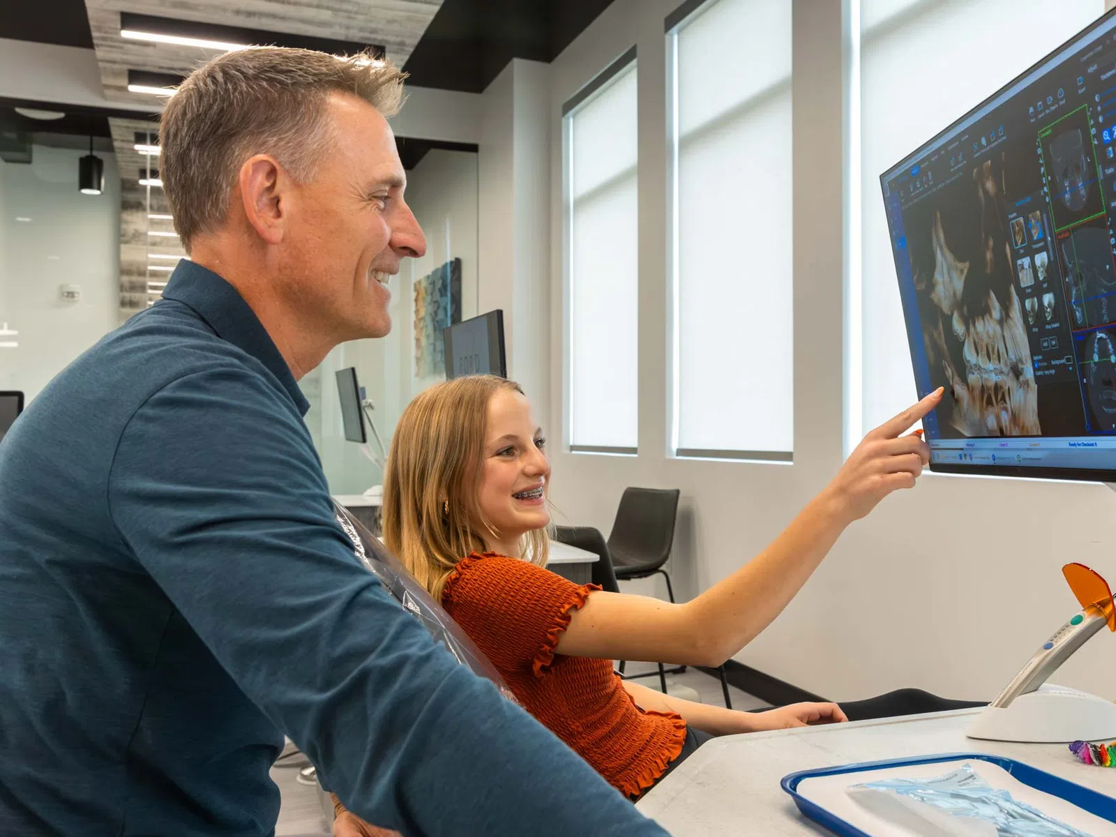 Dentist and girl reviewing dental X-ray images on a large screen in a modern clinic room.