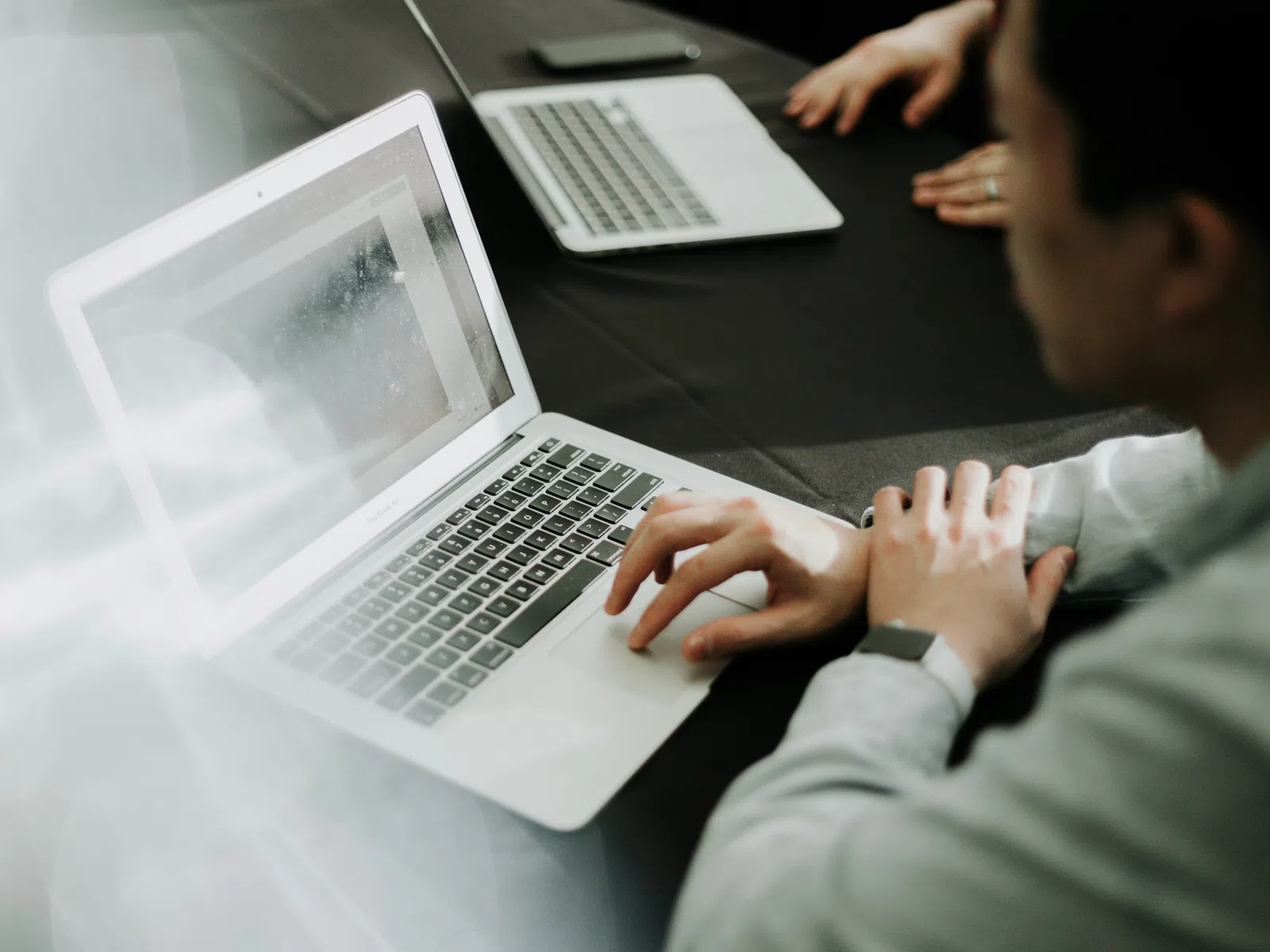 Smiling woman with glasses working on laptop in modern office setting with warm lighting.