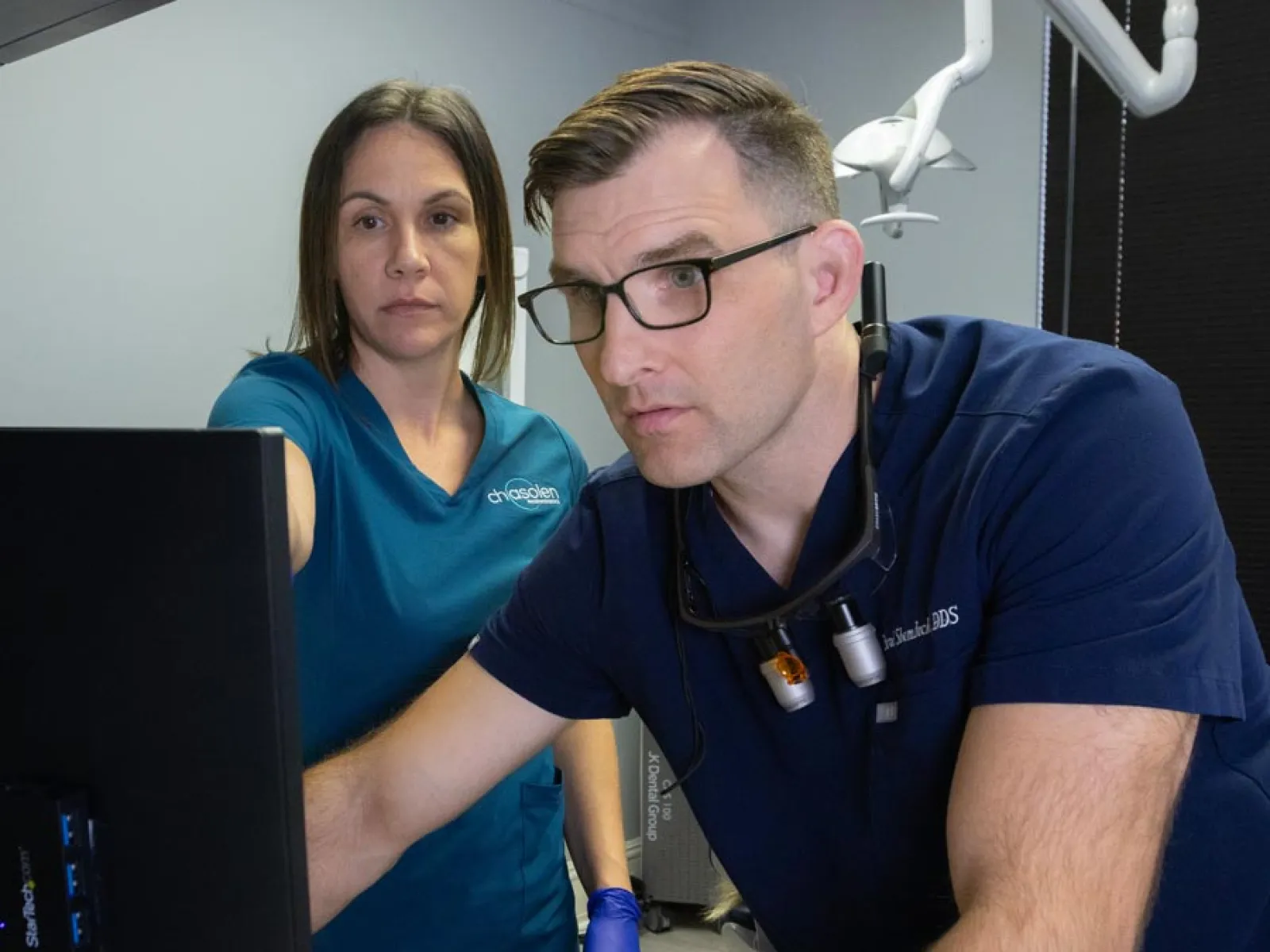 Male and female dental professionals reviewing information on a computer screen in a clinic setting.