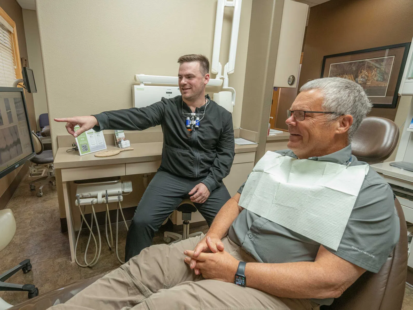 Dentist explaining dental x-rays to a smiling elderly male patient in a modern clinic.