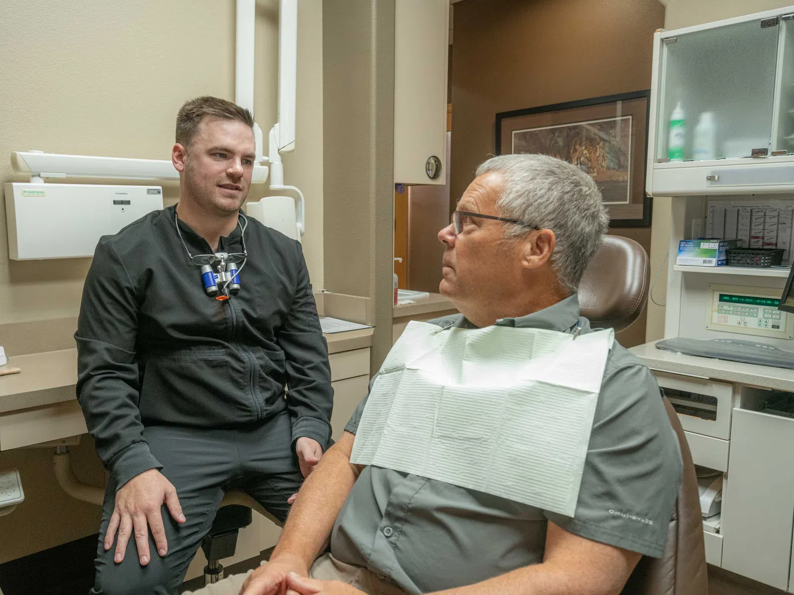 Dentist in dental clinic consulting middle-aged male patient wearing a dental bib in examination chair