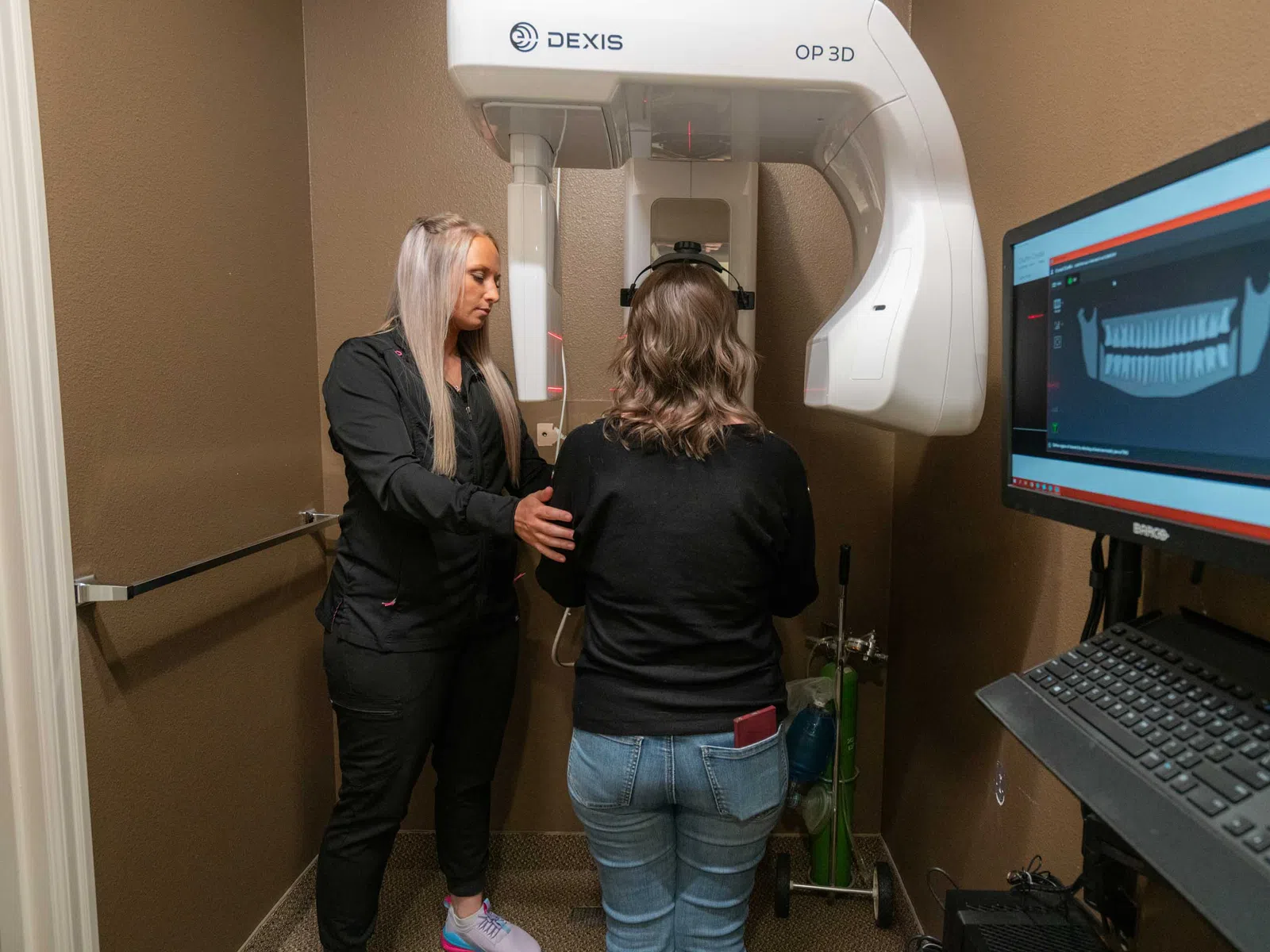 Dental technician assisting patient using 3D dental X-ray machine with panoramic oral scan on computer screen