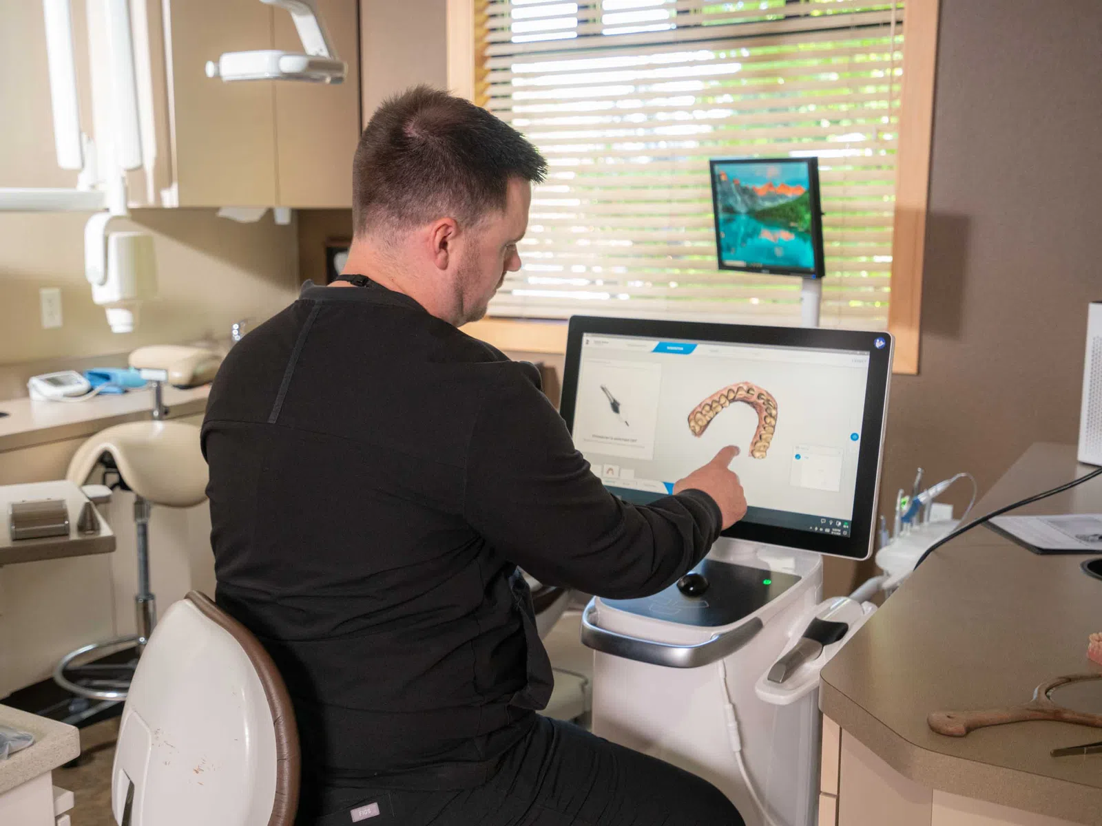 Dentist using digital dental imaging software showing a 3D dental arch model on a computer screen in a modern clinic.