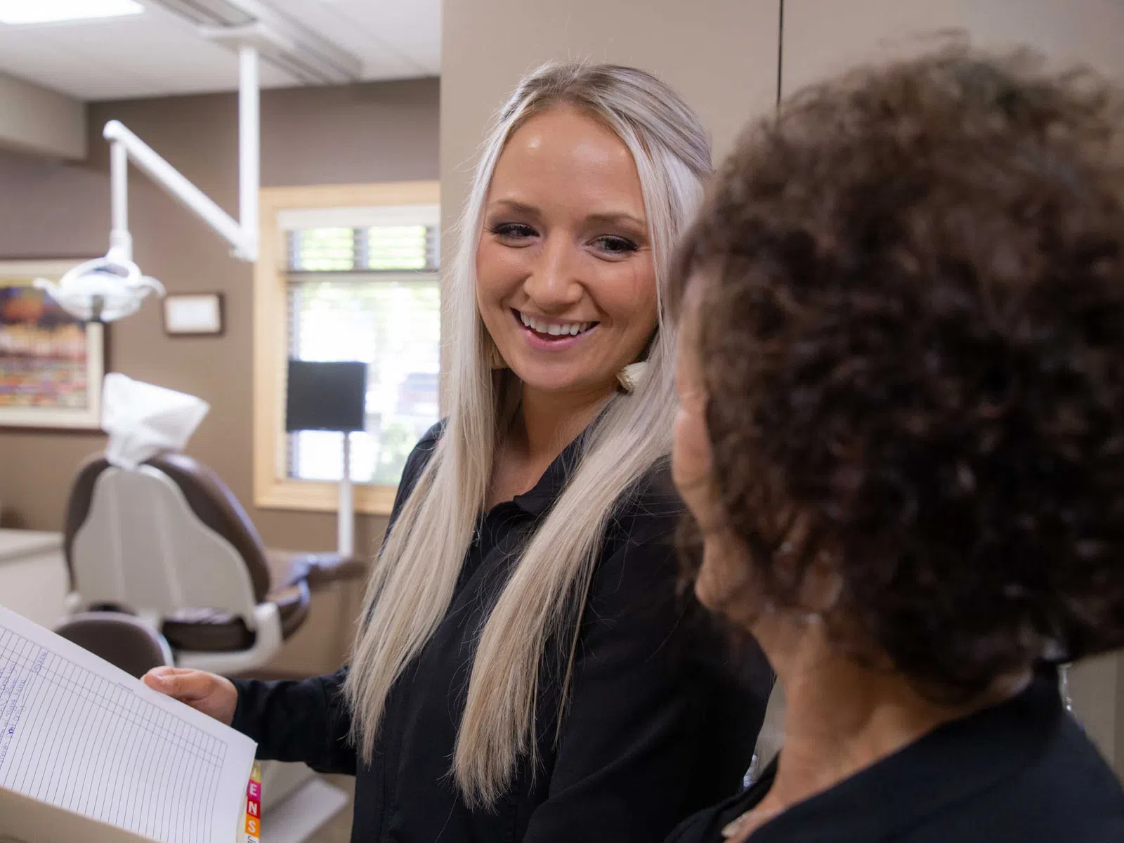 Smiling female dental assistant holding patient chart and talking to a patient in a dental office.
