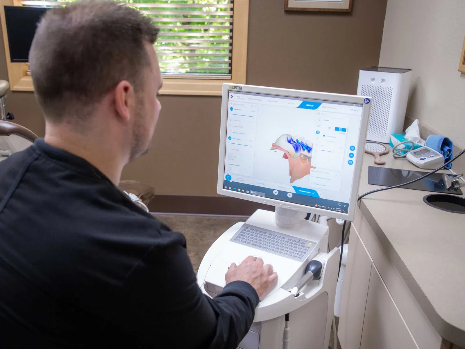 Man using dental software on a computer to analyze a 3D model of teeth in a clinic room.