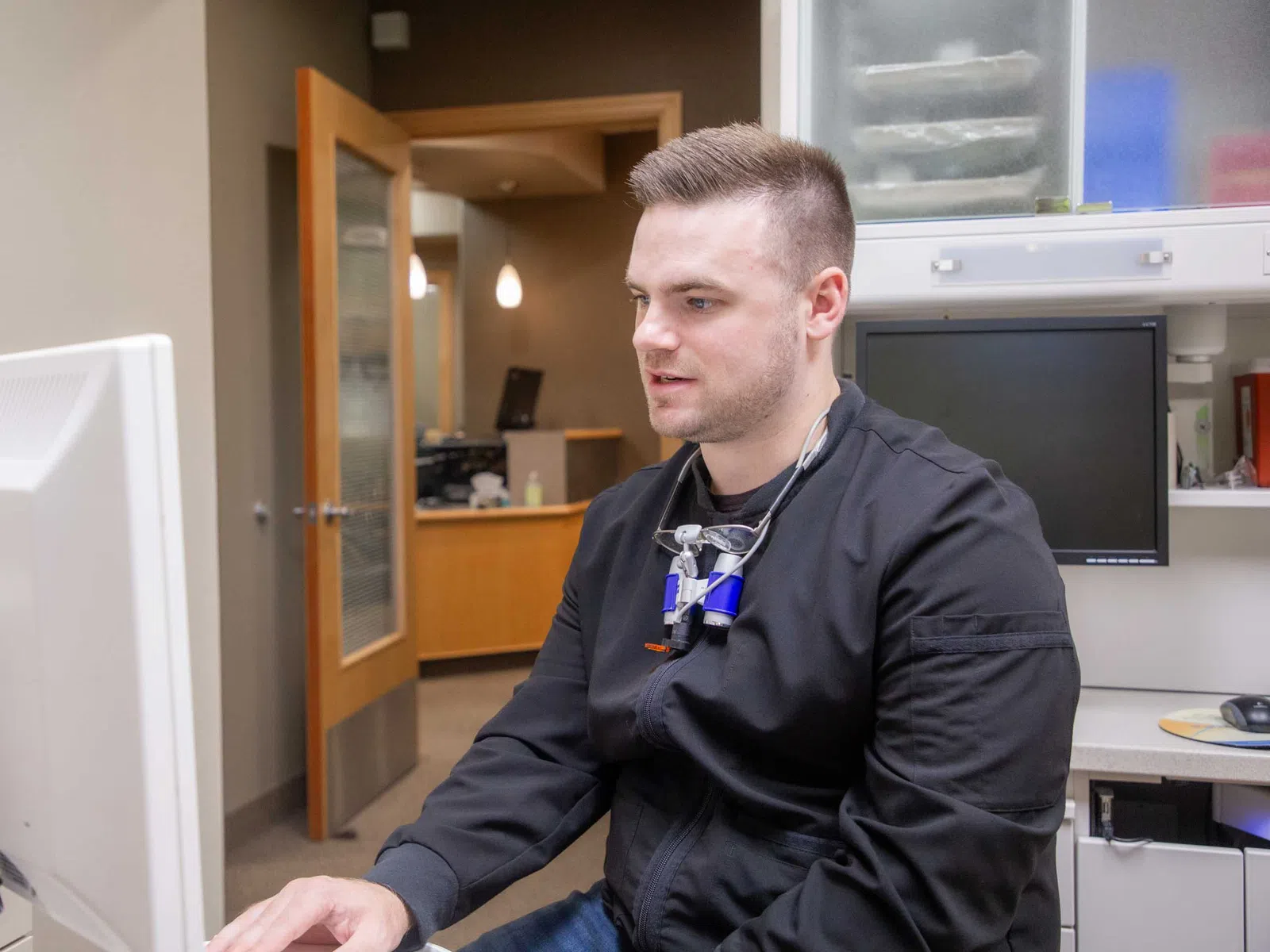 Dentist in black scrubs working on computer in modern dental office with dental tools around
