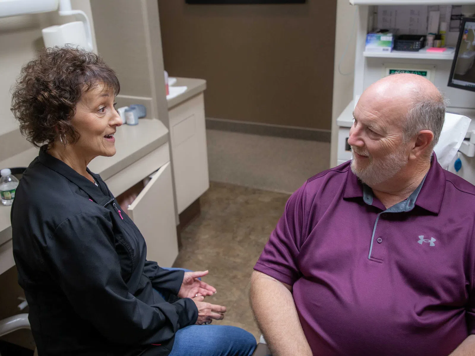 Dentist discussing dental care with a male patient in a modern dental office exam room.