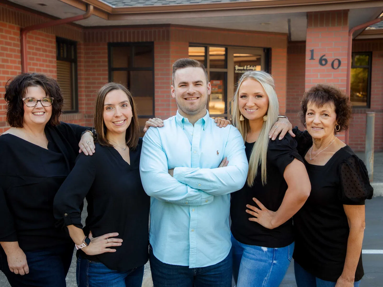 Group of five diverse coworkers smiling and posing outside a brick office building with address 160.