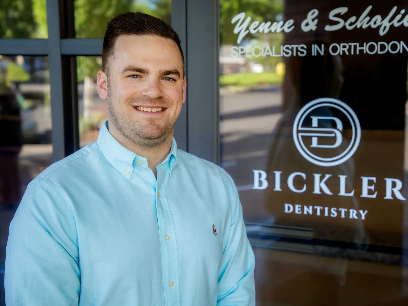 Smiling man in light blue shirt standing outside Bickler Dentistry and Yenne & Schofield orthodontics office