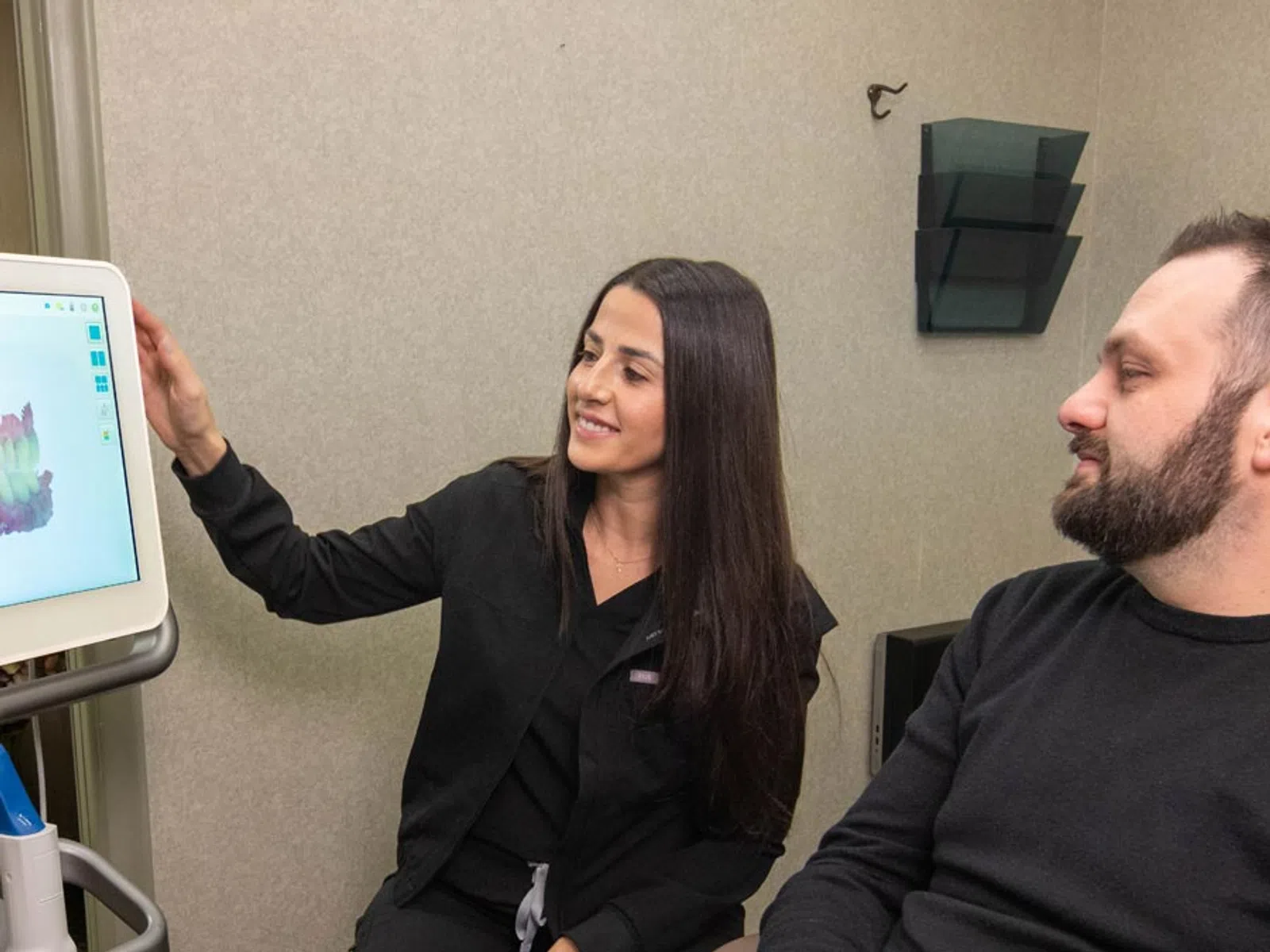 Dental professional explaining 3D dental scan results to a male patient in a clinical setting.