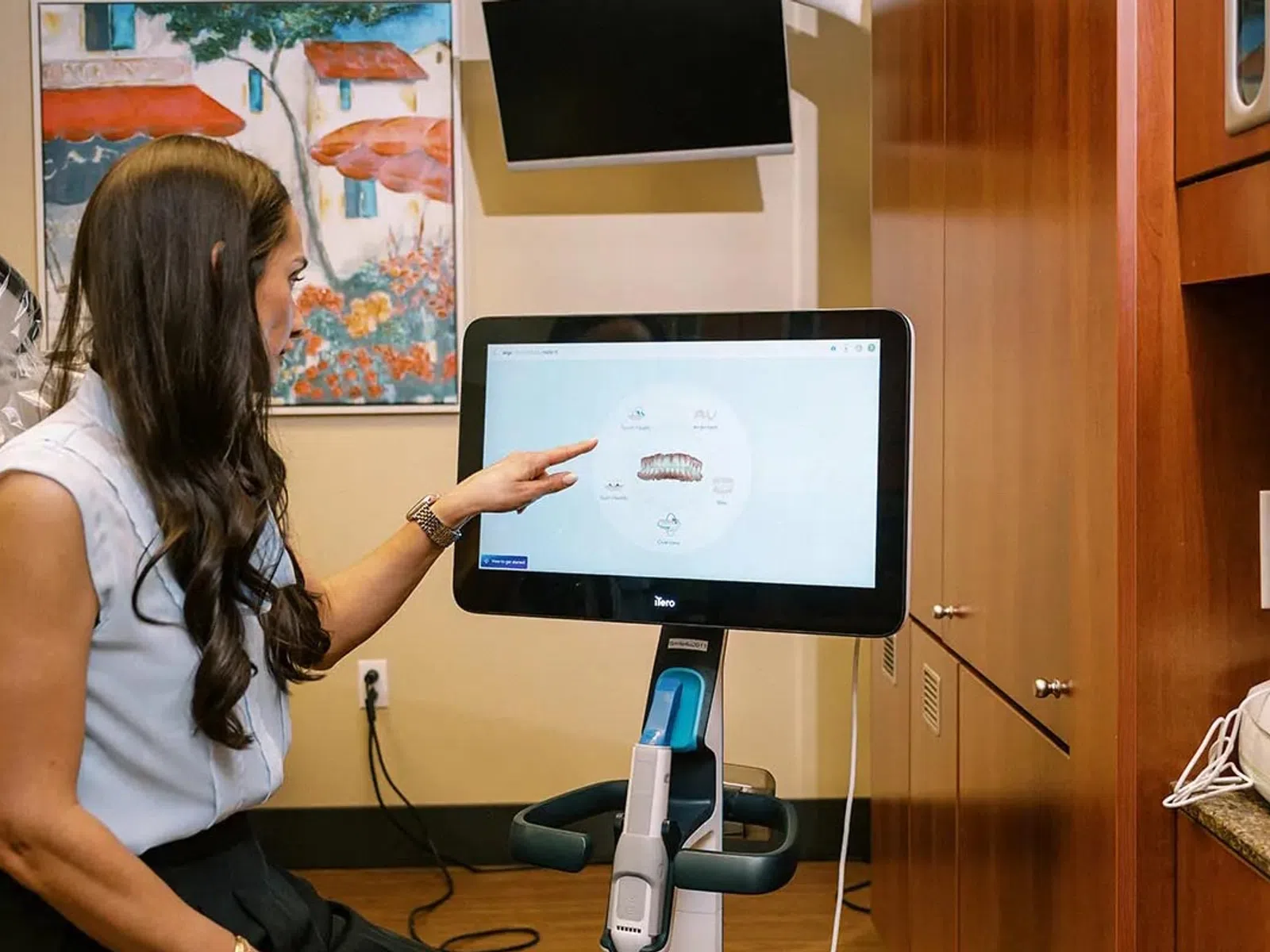Woman pointing at digital dental scan displayed on a large screen in a dental office setting.