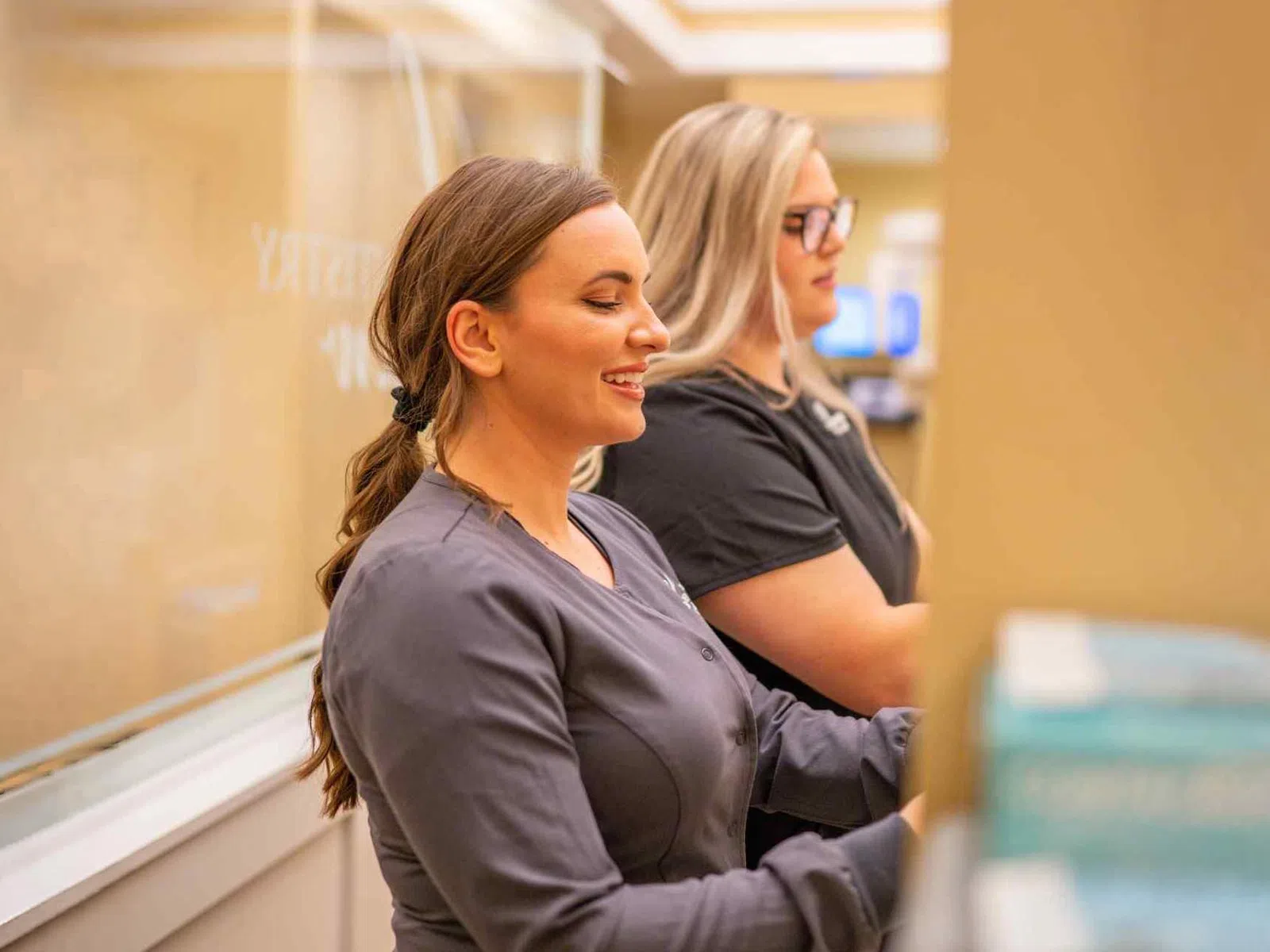 Two women in medical scrubs working at a counter in a healthcare or dental office setting.