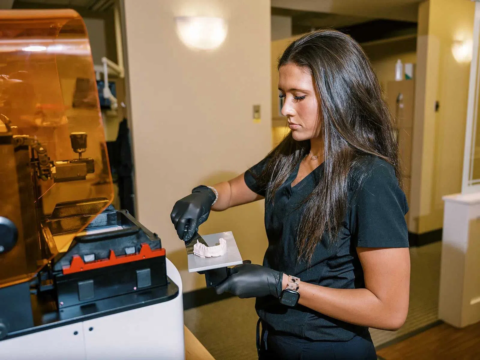 Woman in black scrubs using a 3D printer to create dental molds in a dental lab environment