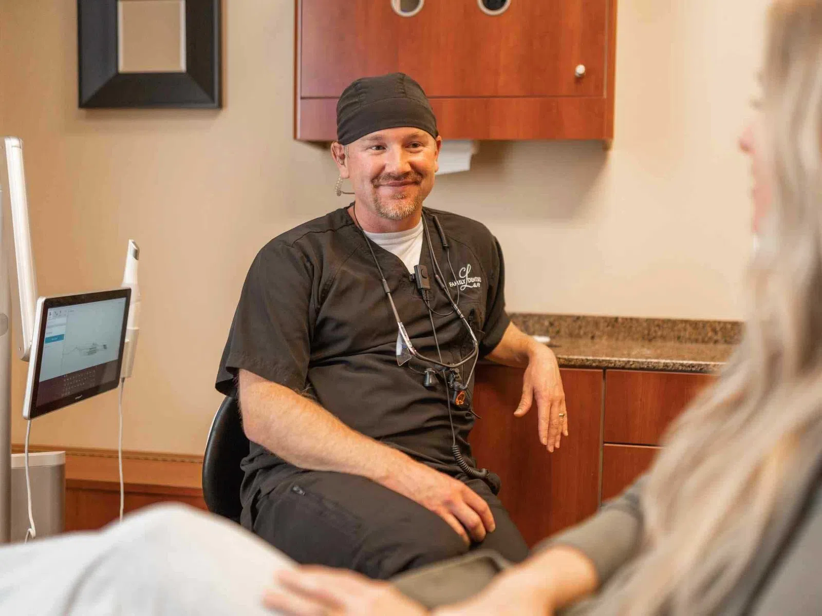 Male dentist in black scrubs consulting with female patient in modern dental office