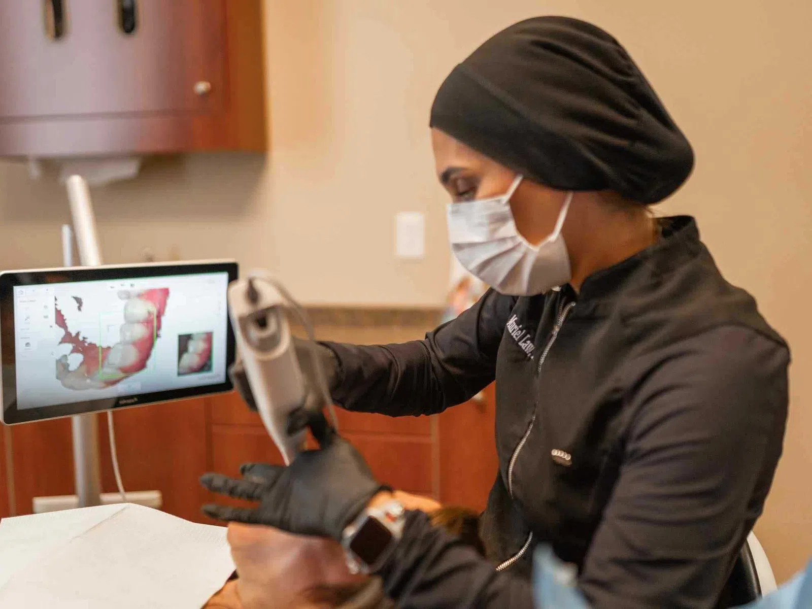 Dentist using a digital scanner for dental impressions with 3D images displayed on a computer screen.