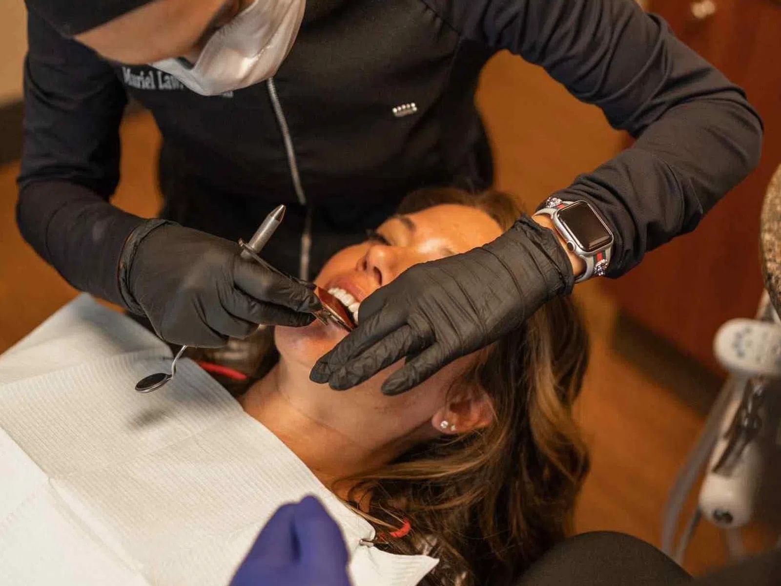 Dentist wearing black gloves treating female patient lying in dental chair with dental tools