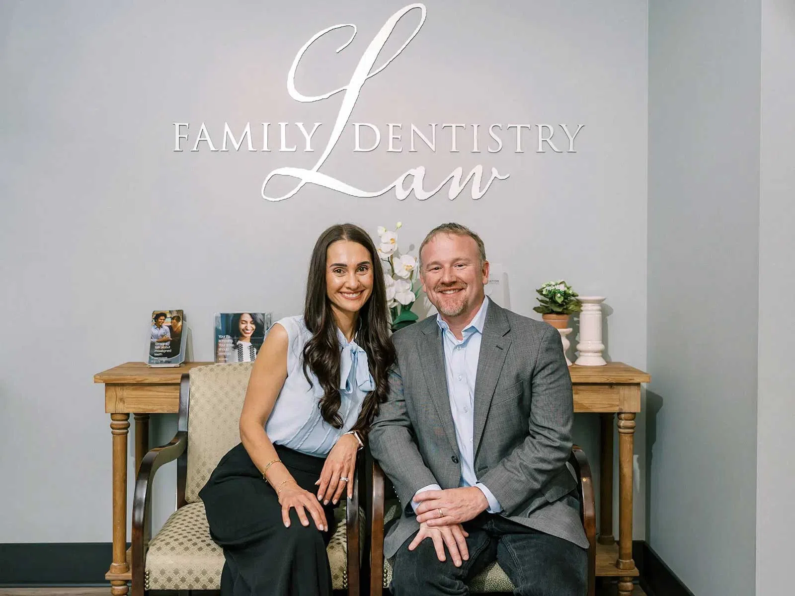 Smiling man and woman seated in a dental office with Family Dentistry Law logo behind them.