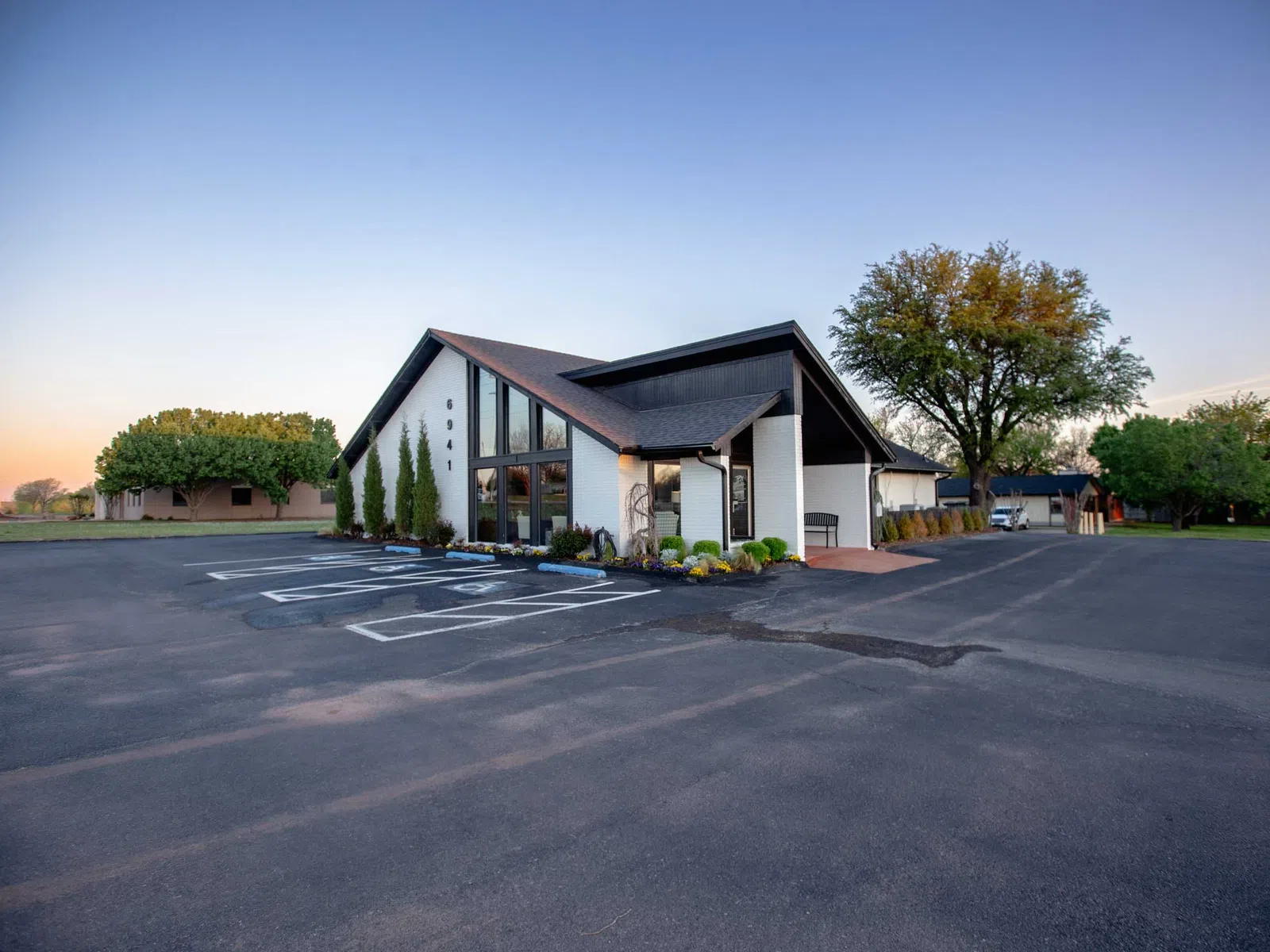 Modern, single-story building with large windows, landscaped front, and spacious parking lot under clear sky.