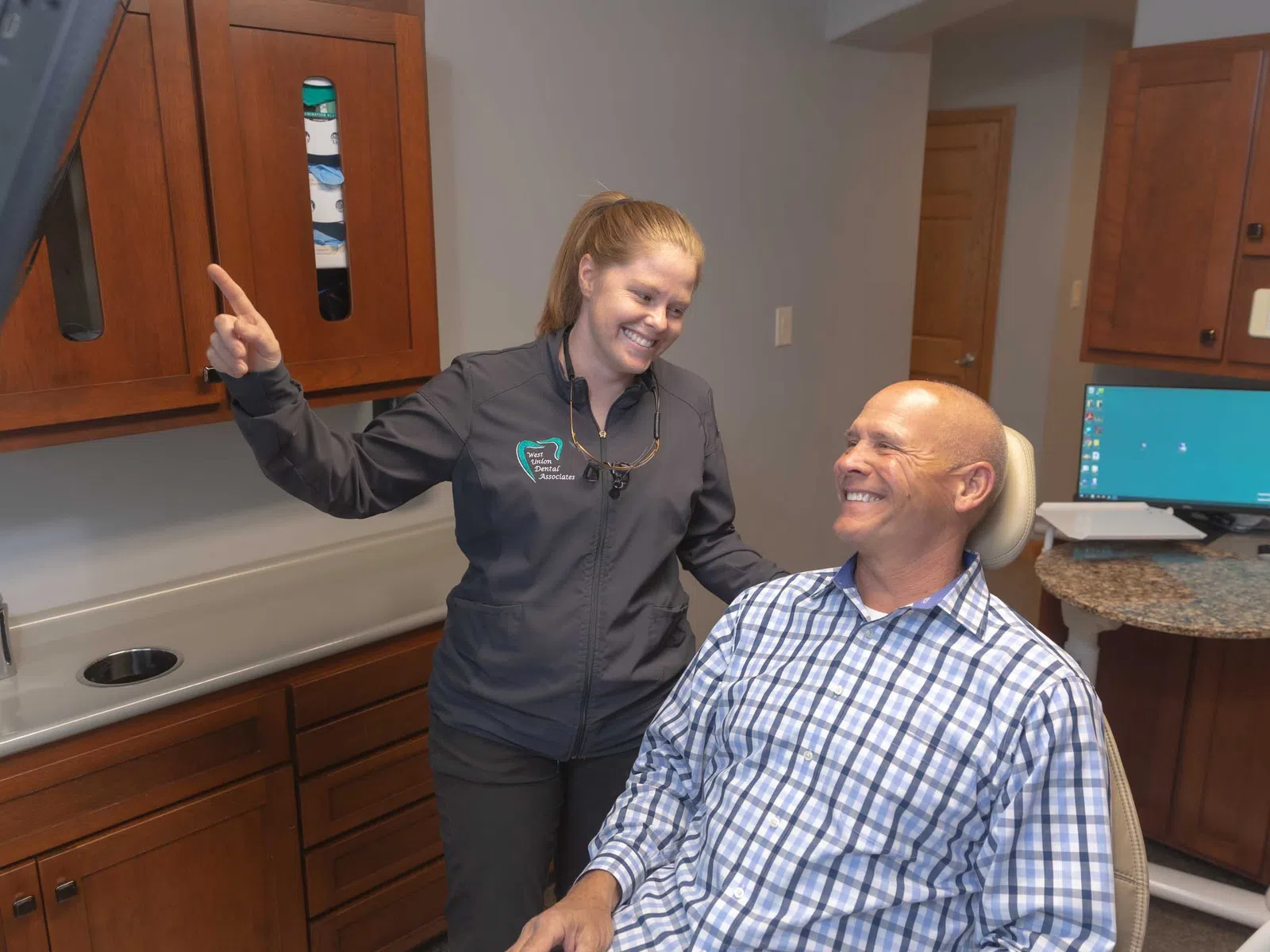 Dentist smiling and explaining treatment to male patient in dental clinic exam room.