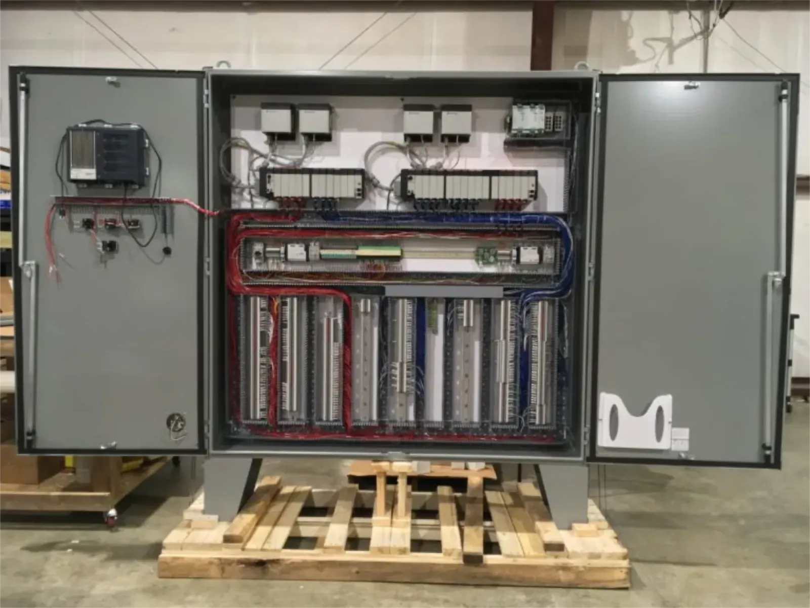 Open industrial control panel with organized wiring and electrical components mounted on pallet in warehouse.