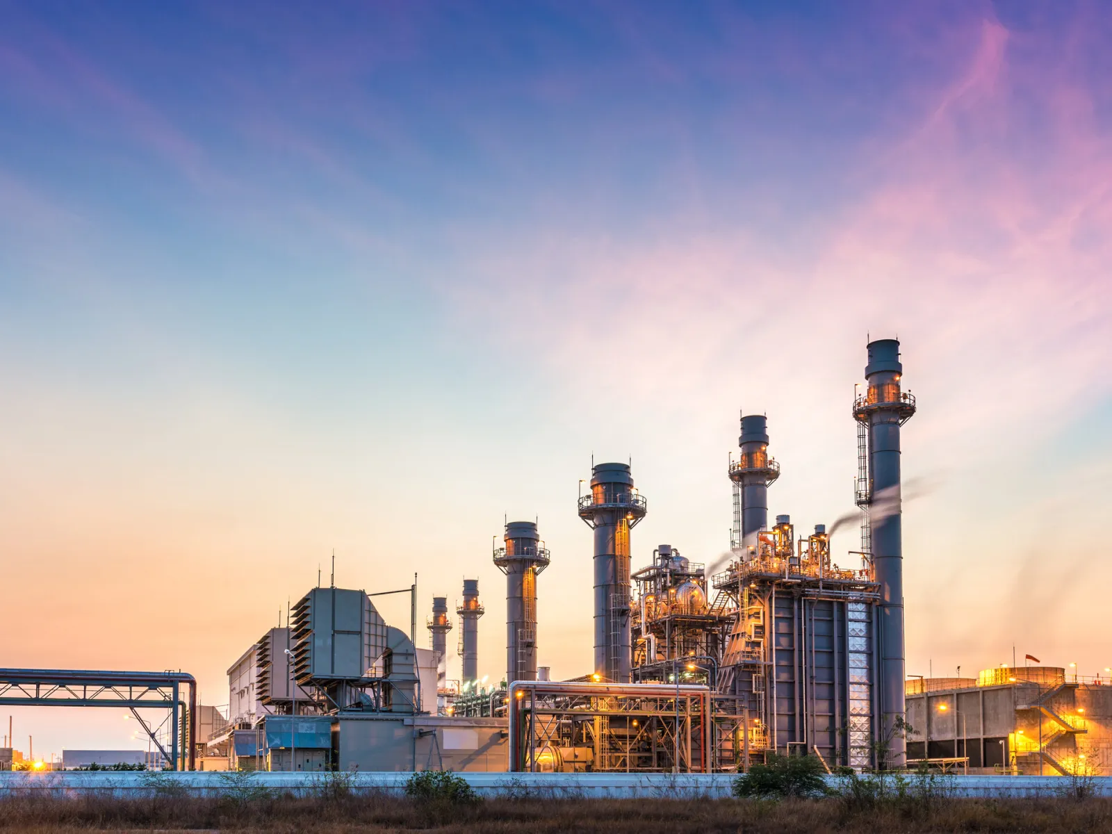 Industrial power plant with tall chimneys and complex structures under a colorful twilight sky.