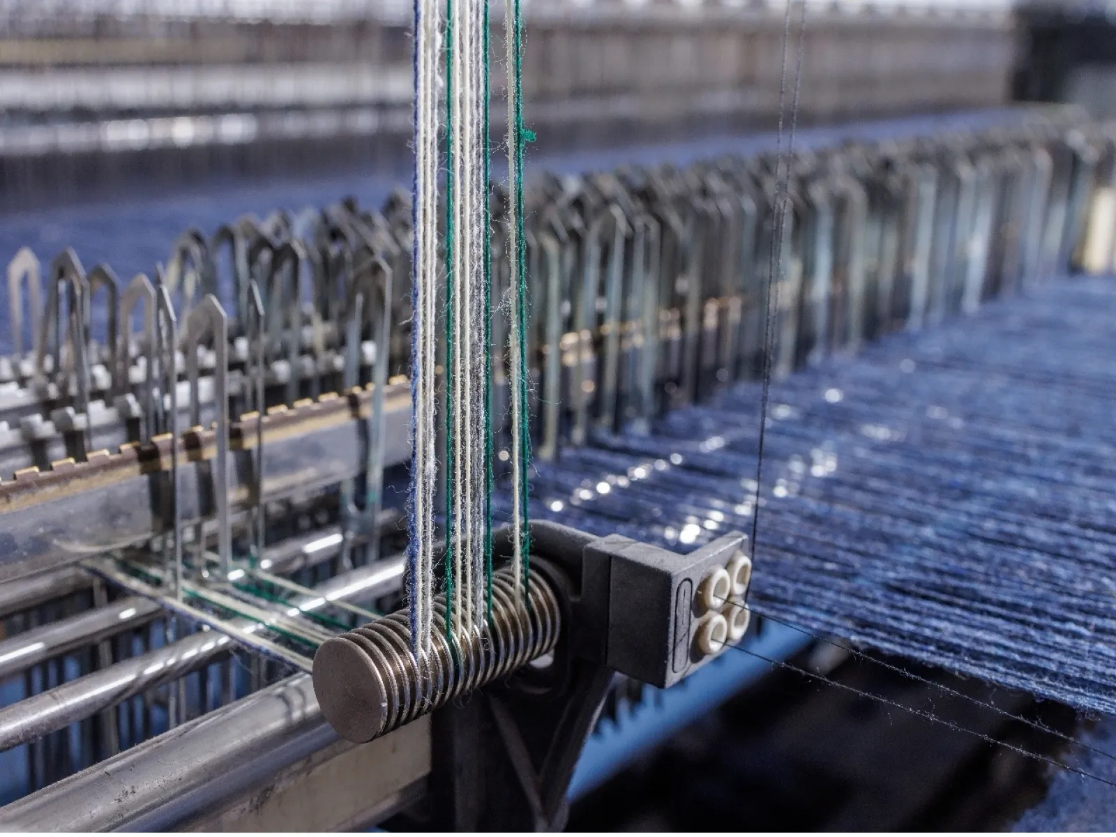 Close-up of industrial weaving machine with blue threads and metal components weaving fabric.