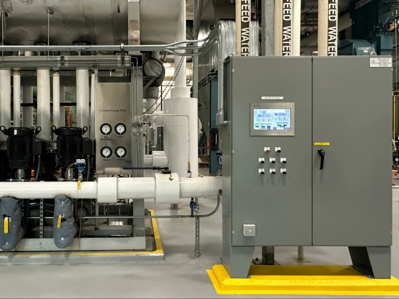 Industrial mechanical room with control panel, piping, gauges, and pumps for water feed system.