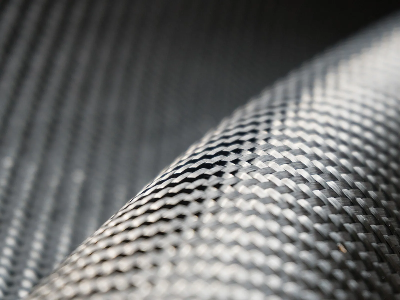 Close-up of woven carbon fiber fabric showing detailed texture and pattern with a glossy finish.