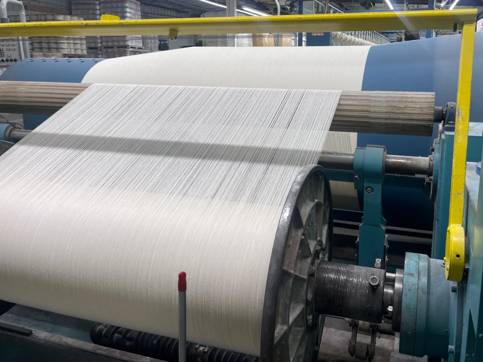 Textile manufacturing machinery winding white fabric yarn in industrial factory setting.