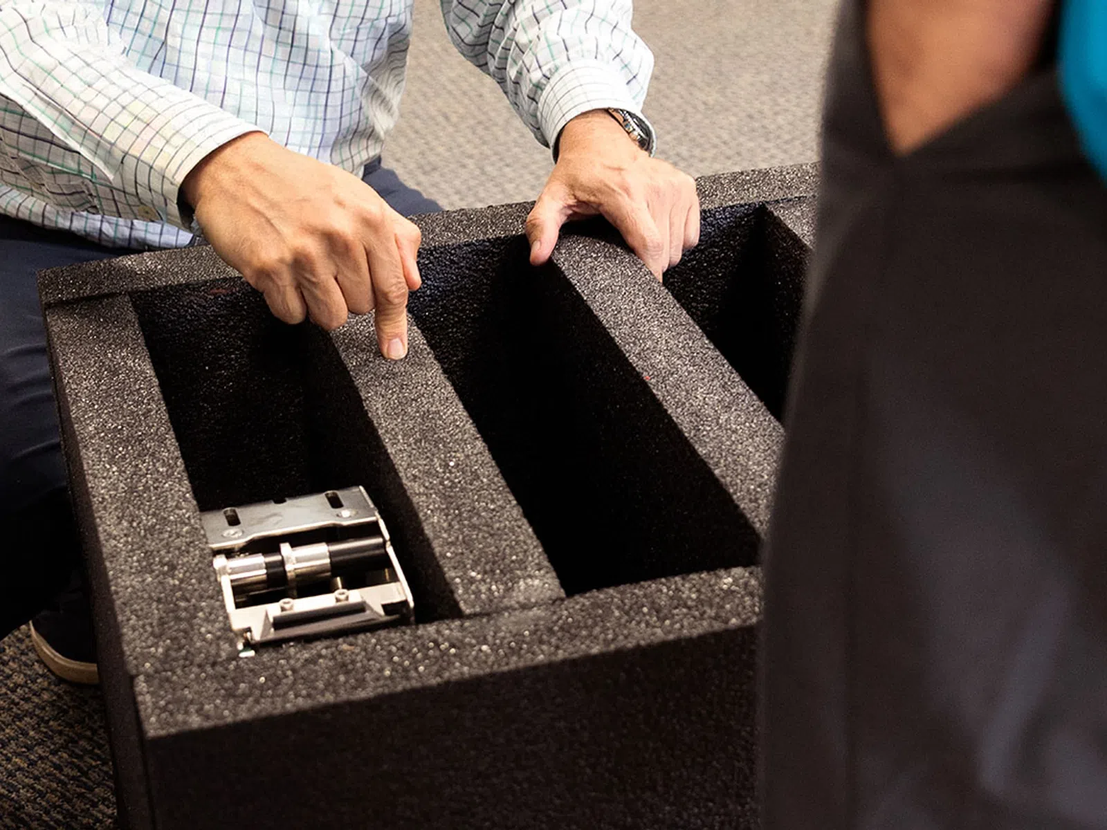 Person showing a foam-lined protective case with divided compartments and a small metallic device inside.