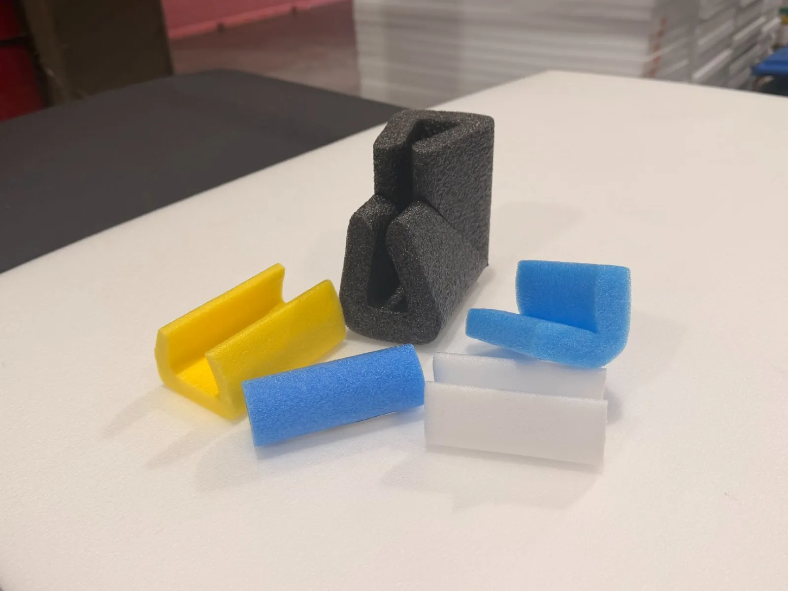 Small foam pieces in various colors and shapes arranged on a white foam board surface indoors.