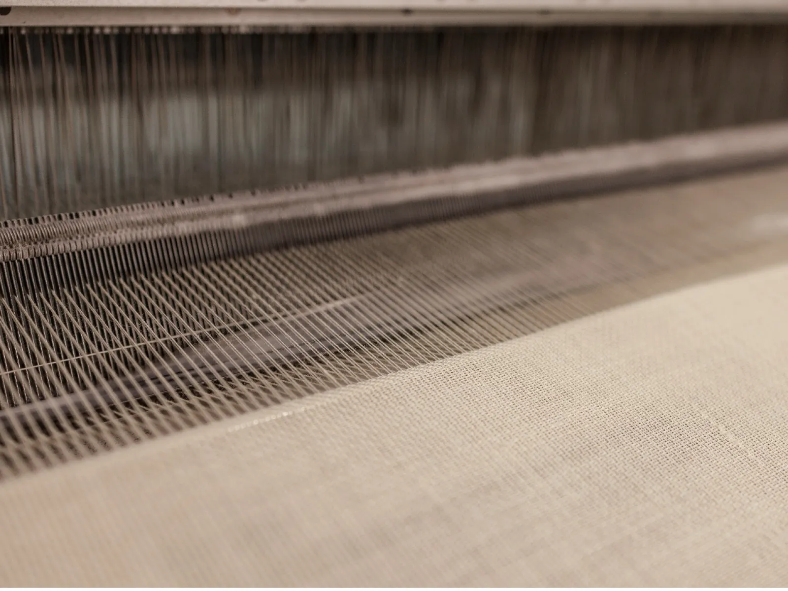 Close-up of an industrial weaving loom creating fine beige fabric with interlaced threads.